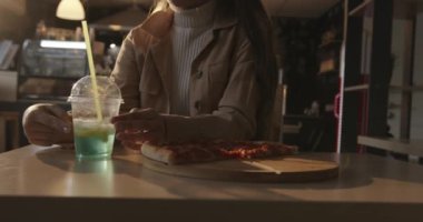 Şehvetli genç kız bir kafede pizzayla masaya oturur ve düşünceli bir şekilde elinde bir kokteylle bardağı çevirir.