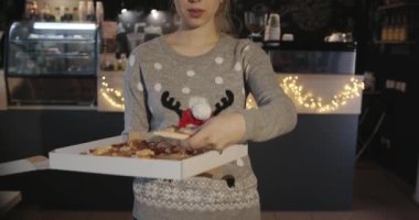 Noel geyiğiyle süveter giyen güzel sarışın kız kafedeki bir kutudan mandalina dilimleriyle süslenmiş pizza yiyor.
