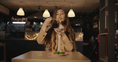 Bej ceketli, yeşil tobiko havyarlı suşi yiyen ve soya sosuna batırıp çubukla tutan tatlı bir genç kız.