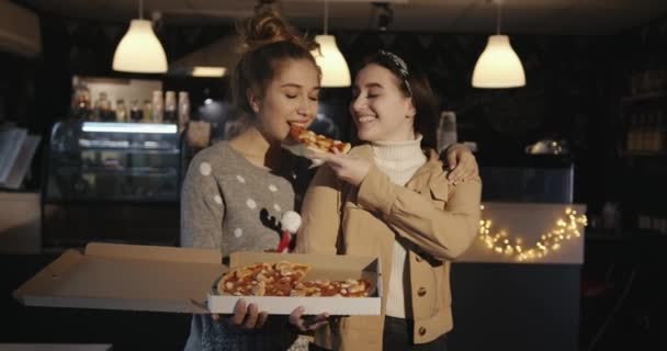 Deux adorables jeunes filles mangent la pizza d'une boîte dans un café et rient contagieusement. Mouvement lent — Video