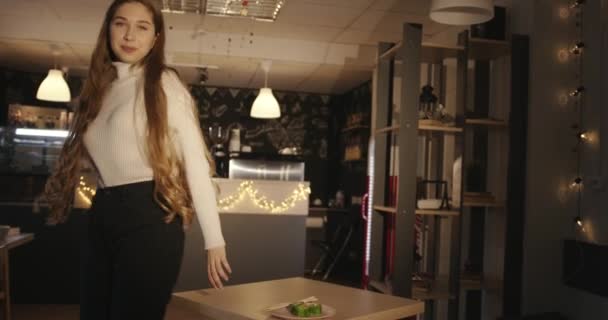 Een teder jong meisje in een witte trui en zwarte jeans zit op een tafel in een café en eet sushi in groene vliegende vis kaviaar — Stockvideo
