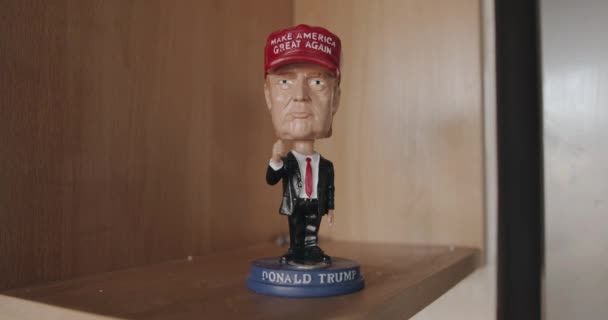 Minsk, Vitryssland - 17 september 2020: En figur av Donald Trump i kostym och en röd mössa står på en trähylla i rummet — Stockvideo