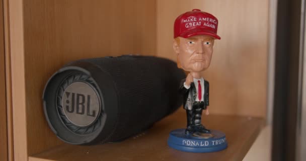 Minsk, Belarus - September 17, 2020: A statuette of Donald Trump in a red cap stands on a wooden shelf against the background of a portable speaker — Stock Video