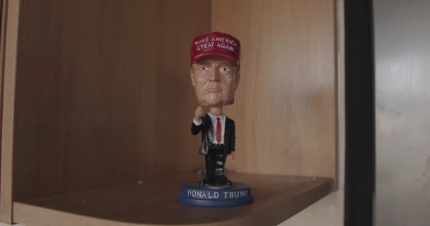 Minsk, Bielorrússia - 17 de setembro de 2020: Estatueta de lembrança de Donald Trump de terno com um laço vermelho e um gorro vermelho em pé em uma prateleira de madeira. Close-up — Vídeo de Stock