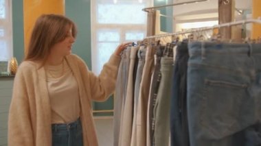 Çekici bir genç kız bir giyim mağazasında alışveriş yaparken raflardaki eşyalara dokunuyor.