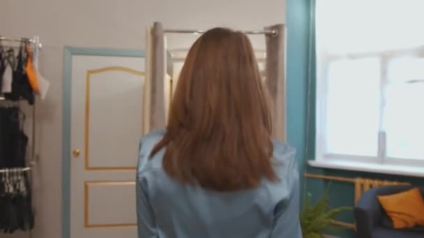 Чувственная молодая девушка демонстрирует модный бант в магазине одежды и входит в примерочную комнату, задергивая шторы — стоковое видео