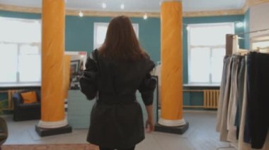 Çekici bir genç kız giyim mağazasından alışveriş yaparken şık bir görünüm sergiliyor ve soyunma odasına girip perdeleri çekiyor.