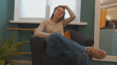 Hippi kıyafetli güzel genç kız bir moda butiğinin koltuğunda oturuyor ve kameraya poz veriyor.