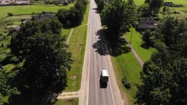 Otoyolda giden bir minibüsün üst görüntüsü ve bir yaz günü yol boyunca arka bahçeli köyün özel evleri.