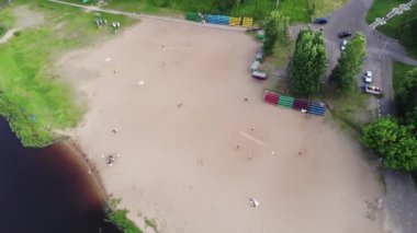 Yazın kumlu bir sahilde dinlenen insanların hava manzarası ve rıhtımdaki nehir kıyısında bir tekne.