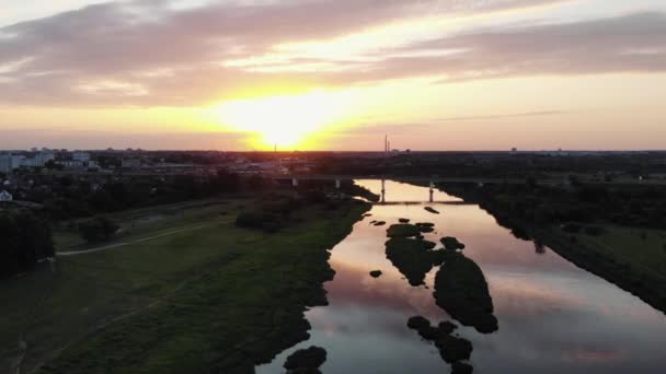 Fantastiska drönare bilder av en stad på flodstranden med gröna öar i mitten och en väg bro mot bakgrund av solnedgången — Stockvideo