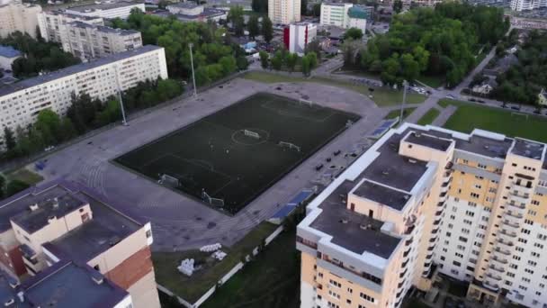 Vista superior del entrenamiento de los deportistas de un club de fútbol en el estadio y panorama de los barrios residenciales de la ciudad en una noche de verano — Vídeos de Stock