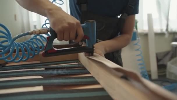 Misk, Belarus - May 15, 2020: The master nails the upholstery to the wooden frame of the sofa with a pneumatic stapler in the upholstered furniture repair workshop — Stock Video