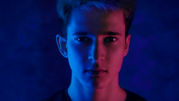 Portret przystojnego młodego mężczyzny na czarnym tle w neonowym świetle i czerwonym świetle migającym na jego twarzy. Wideo 4K — Wideo stockowe