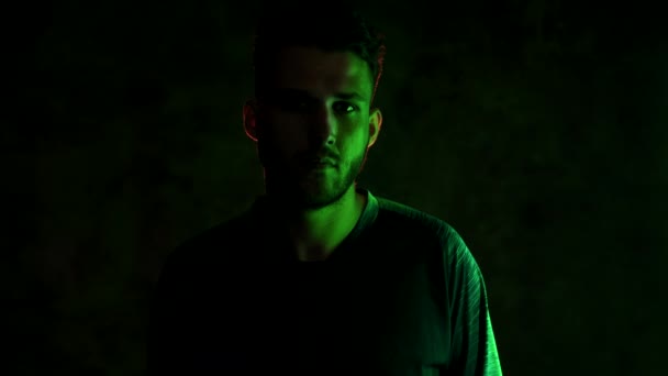 Portrait d'un jeune sportif barbu brutal dans une pièce sombre éclairée au néon, les mains pliées sur la poitrine. 4K — Video