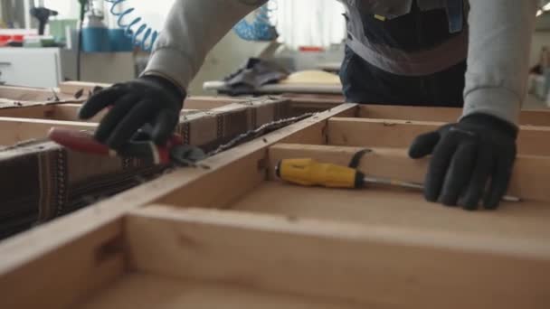 Misk, Białoruś - 15 maja 2020: Mężczyzna w czarnych rękawiczkach pracuje w warsztacie naprawczym mebli i wyciąga zszywki z drewnianej ramy starej sofy — Wideo stockowe