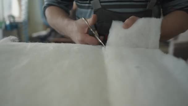 Un homme travaille dans un atelier et coupe l'excès d'hiver synthétique avec des ciseaux dans le processus de réparation de meubles rembourrés — Video