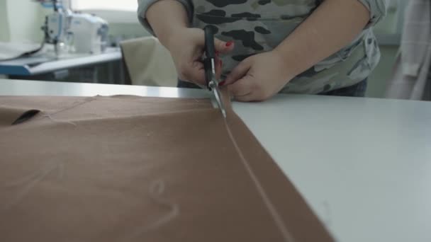 Uma mulher trabalha em um atelier de produção e corta o tecido com tesoura ao longo das linhas desenhadas com giz — Vídeo de Stock
