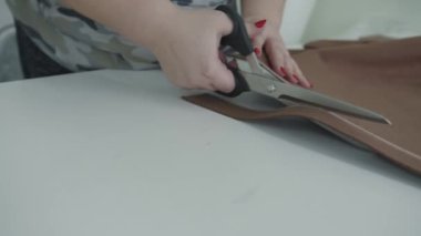 Bir terzi bir üretim atölyesinde çalışır ve bitmiş ürünü dikmek için tebeşirle çizilmiş bir çizgi boyunca makas ile kumaşı keser.