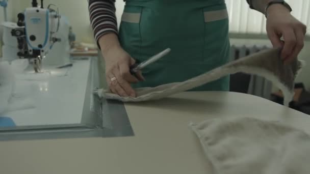 A woman on the background of a professional sewing machine in a workshop cuts off excess fabric on the details with scissors — Stock Video