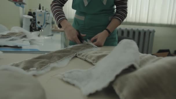 Μια γυναίκα εργάζεται σε ένα εργαστήριο για την επισκευή των επίπλων με ταπετσαρία και κόβει τις λεπτομέρειες ενός καναπέ-κάλυμμα με ψαλίδι — Αρχείο Βίντεο