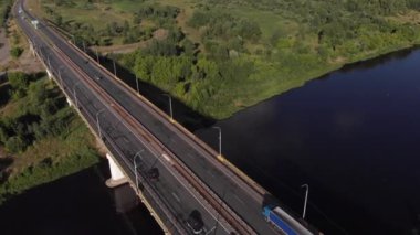 Köprüdeki araba trafiğinin en üst görüntüsü ve bir yaz günü ormanlarla ve çayırlarla çevrili nehrin güzel manzarası.