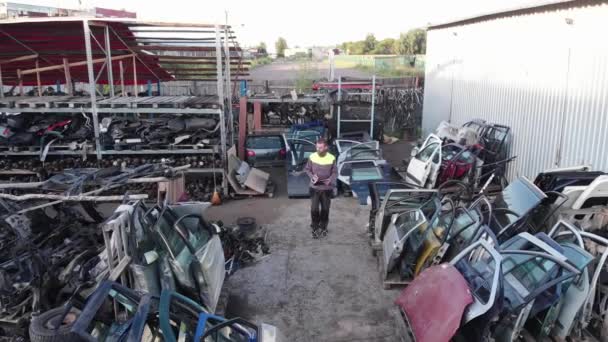 Drone footage of a young bearded auto mechanic with glasses walking through the rows with spare parts for cars and writing in a notebook — Stock Video