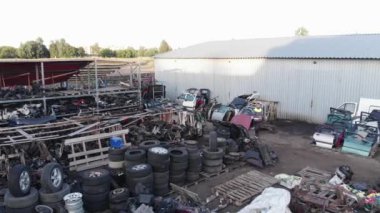 Açık hava deposunda yedek parça sıraları arasında yürüyen genç bir araba tamircisinin hava görüntüsü ve not defteri.