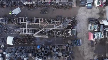 Açık hava deposunda paletlerin üzerinde duran yedek parça için İHA atışları ve sıraların arasında yürüyen genç bir oto tamircisi.