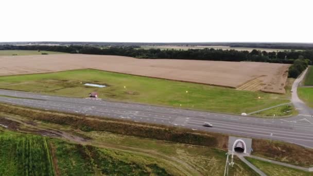 Вид зверху на пшеничне поле в сільській місцевості і широке шосе з дорожніми розмітками і автомобілями, що проходять уздовж неї — стокове відео