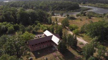 Nehrin kıyısındaki ağaçların arasında duran ve doğada dinlenen haç şeklinde büyük bir evi olan bir malikanenin en üst görüntüsü.