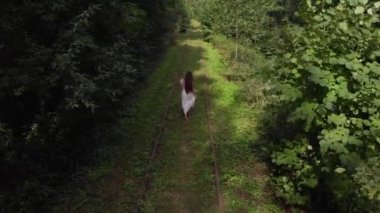 Terk edilmiş bir yaz ormanında çıplak ayakla yürüyen beyaz elbiseli genç bir kızın hava manzarası.