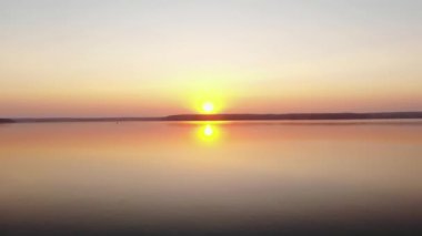Devasa bir göl üzerinde gün batımının göz kamaştırıcı hava manzarası ve pembe gökyüzünün ve güneşin sudaki yansıması.