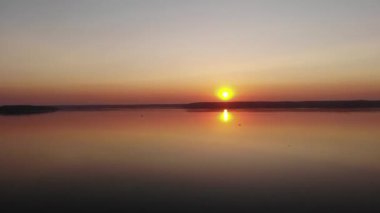 Ormanlarla çevrili bir gölün üzerinde yaz günbatımının drone 'undan çekim yapmak ve sudaki güneşten turuncu bir yol.