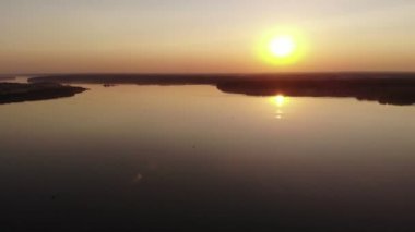 Gün batımında turuncu bir güneş ve ufkun ötesine uzanan ormanları olan büyük bir göl ile gökyüzünün insansız hava aracı atışları.