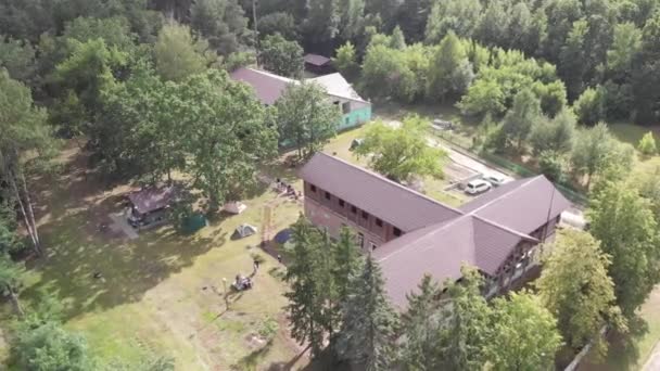 Birds-eye view van een huis in de vorm van een kruis in het bos en een groep mensen in de buurt van tenten op het gras op zomervakantie — Stockvideo