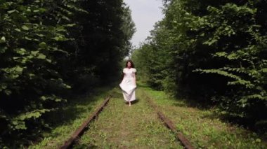 Beyaz elbiseli güzel bir genç kız ormanda terk edilmiş eski bir demiryolu boyunca yalınayak koşuyor. Hava görünümü