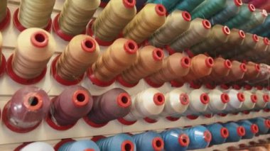 Dikiş makineleri için sıra sıra iplik makaraları bir üretim manufabrikasında ya da elbise dikmek için atölyede büyük stantlar üzerinde duruyor