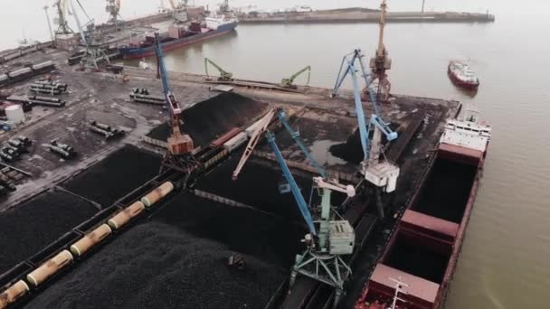 Вид зверху на завантаження вугілля баштовими кранами в танкери на території морського порту і плавучі кораблі в бухті — стокове відео
