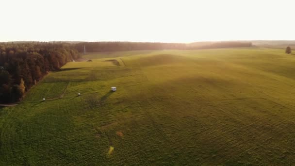 Vista aérea da deslumbrante paisagem de verão e reboque em pé em prados montanhosos cercados por floresta ao pôr do sol — Vídeo de Stock