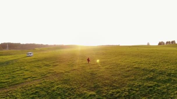 Yeşil tepecikli çayırlarda kolları gün batımına karşı açık koşan genç kızın hava manzarası. Özgürlük kavramı — Stok video