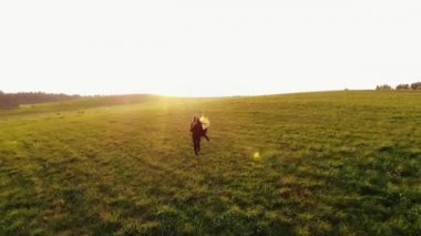 Genç, uzun saçlı bir kızın uzaktan kumandalı uçağıyla gün batımının arka planına doğru koşuyor.