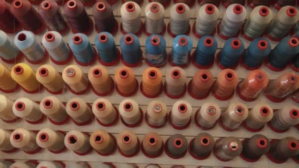 Top view of rows of spools of thread for sewing in different colors and shades on a rack in a production workshop or atelier — Stock Video