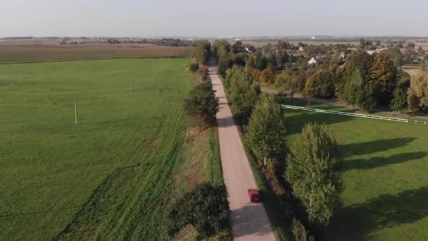 Veduta aerea di una macchina su una strada sterrata nella campagna vicino a un villaggio circondato da alberi verdi e campi — Video Stock