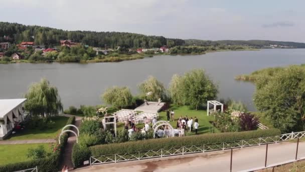 Veduta aerea di un prato verde decorato per la cerimonia nuziale e un baldacchino per gli ospiti lungo il fiume in una giornata estiva — Video Stock