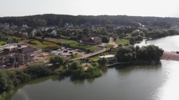 Un pueblo rural con cabañas en la orilla del río y un área al aire libre decorada para la ceremonia de la boda. Vista desde arriba — Vídeos de Stock