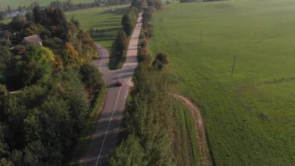 一辆红色汽车沿着大路驶过一个村庄，在美丽的风景背景下驶过一条河。从上面看 — 图库视频影像