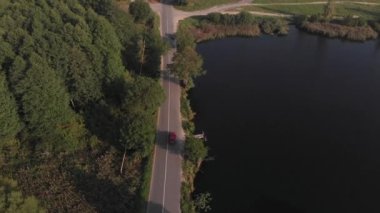 Araba, güzel bir yaz kırsal kesiminde nehir boyunca yol boyunca sürer. Yukarıdan görüntüle