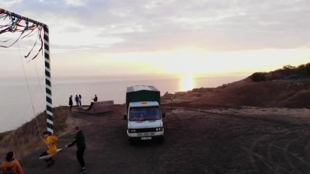 Taganrog, Rusia - 21 de mayo de 2020: Vista aérea de la puesta de sol sobre el mar y la gente en el sitio en una colina con columpios de cuerda y coches — Vídeos de Stock