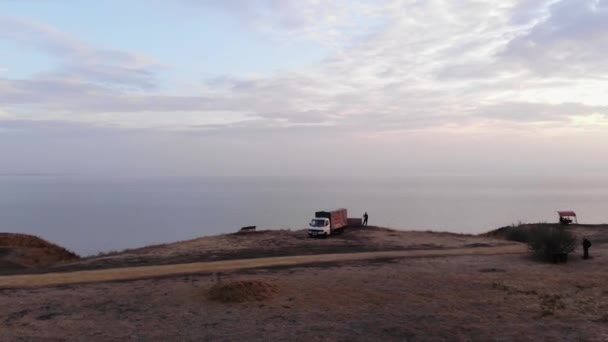 Tepedeki tatilciler gün batımındaki sakin denize ve deniz feneriyle sahilin manzarasına hayran. Hava görünümü — Stok video